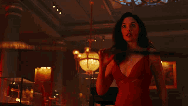 a woman in a red dress is holding a spear in a dark room