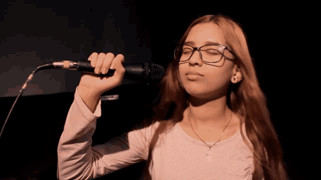 a girl with glasses singing into a microphone with her eyes closed
