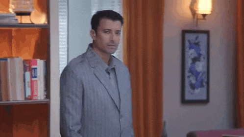 a man in a suit is standing in front of a bookshelf .