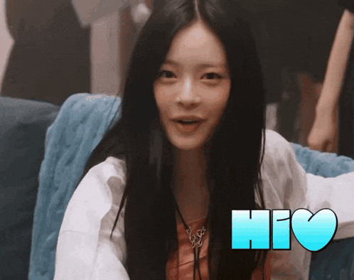 a woman with long black hair is sitting on a couch next to a heart that says hio on it