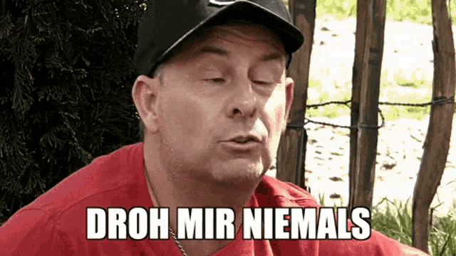 a man wearing a red shirt and a hat says droh mir niemals