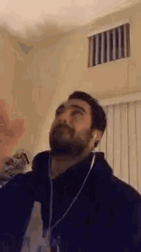 a man with a beard is wearing headphones and waving in a room .
