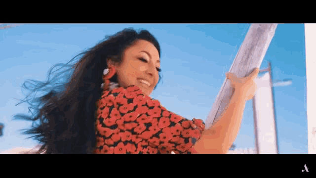 a woman in a red floral dress is smiling and holding a wooden pole