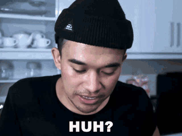 a man wearing a black beanie and a black shirt has the word huh on his shirt
