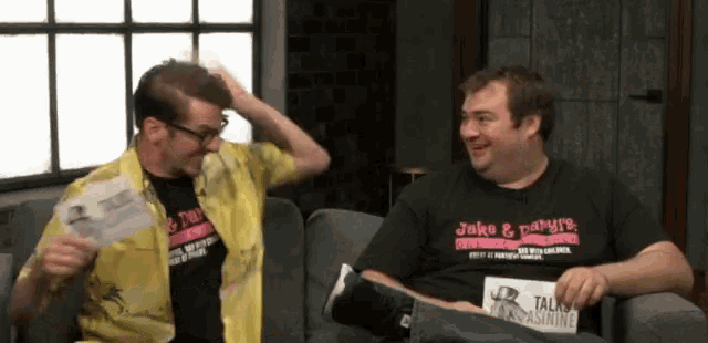 two men are sitting on a couch and one has a shirt that says jake & vampire on it