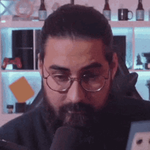 a man with a beard and glasses is sitting in front of a microphone in a room .