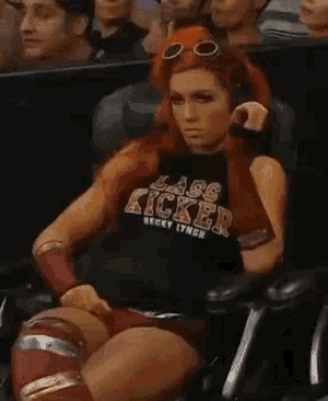 a woman is sitting in a chair wearing a black shirt that says lass kicker on it .