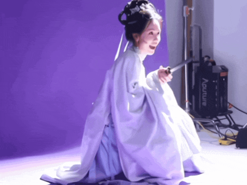 a woman in a white dress is holding a sword in front of an aputure machine