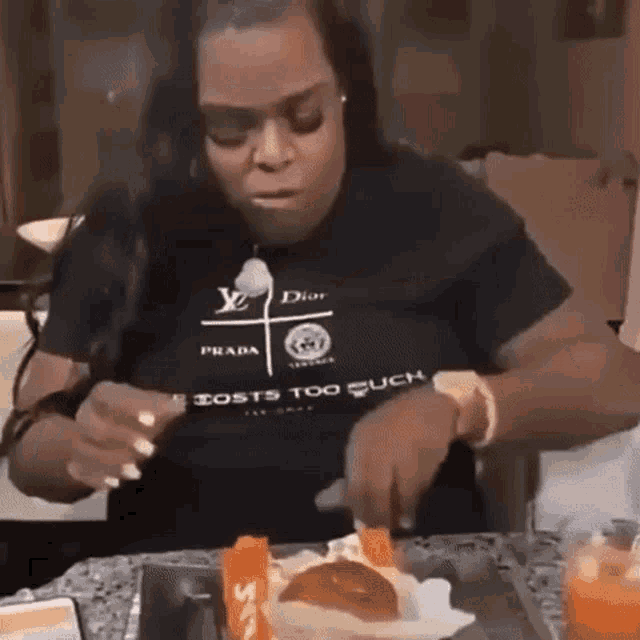 a woman is sitting at a table eating a hamburger while wearing a prada t-shirt .