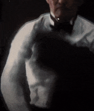 a man in a tuxedo and bow tie is standing in the dark holding a person .
