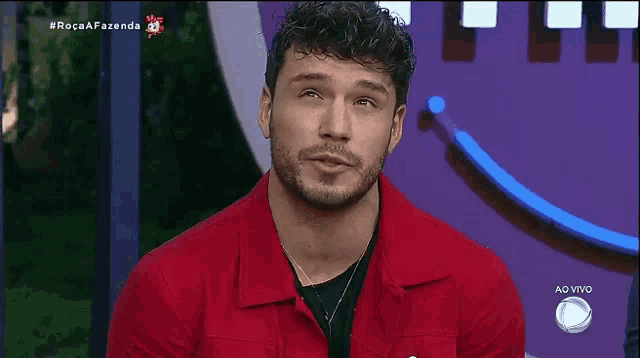 a man in a red shirt is sitting in front of a screen that says ao vivo on it