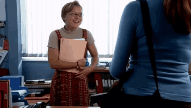 a woman in a blue sweater is standing next to a woman holding a folder