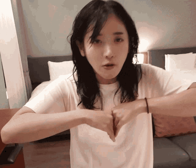 a woman in a white t-shirt is making a heart shape with her hands