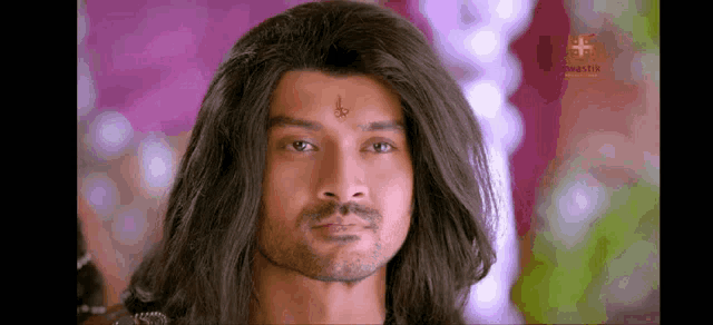 a man with long hair and a tattoo on his forehead looks at the camera .