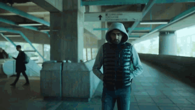 a man in a hooded jacket is standing in a hallway with a sign that says ' railway station '