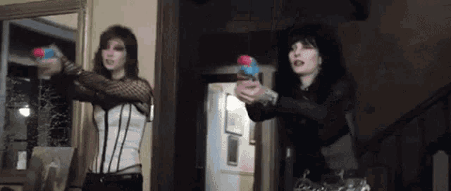 two women are holding water guns in front of a mirror .