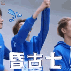 a group of young men wearing blue sweatshirts are raising their hands in the air .