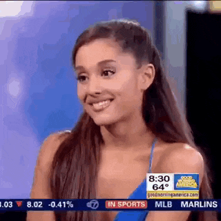 ariana grande is smiling while sitting in front of a screen that says in sports .
