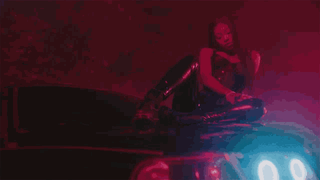 a woman is sitting on the hood of a car with a red light behind her