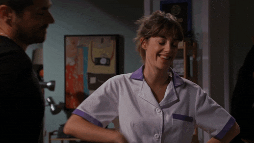 a woman in a white and purple uniform smiles while a man looks on