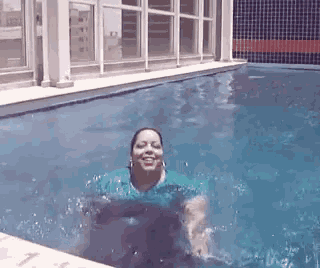 a woman in a blue shirt is swimming in a pool and smiling