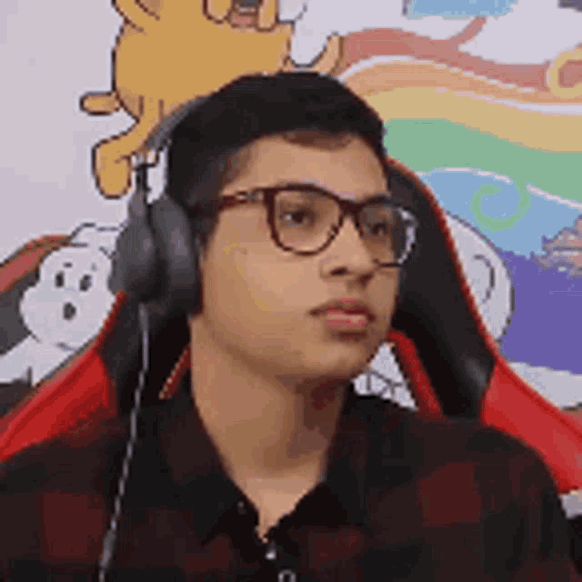 a young man wearing headphones and glasses is sitting in front of a cartoon .