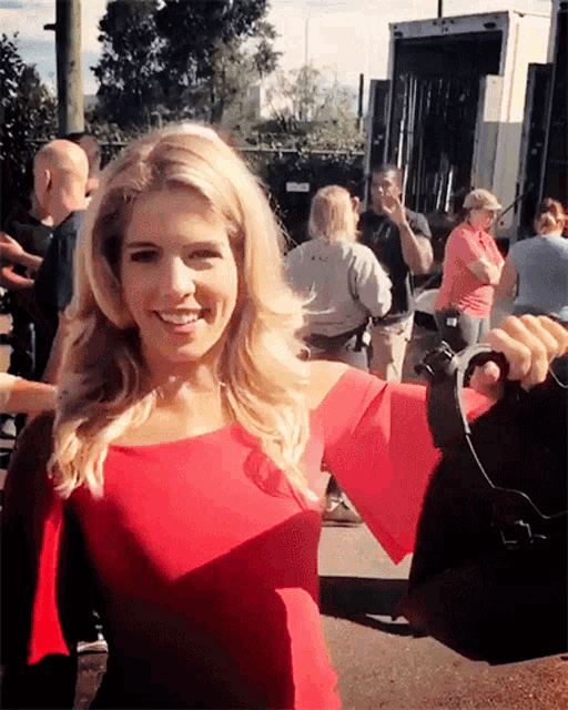 a woman in a red top is smiling in front of a crowd of people