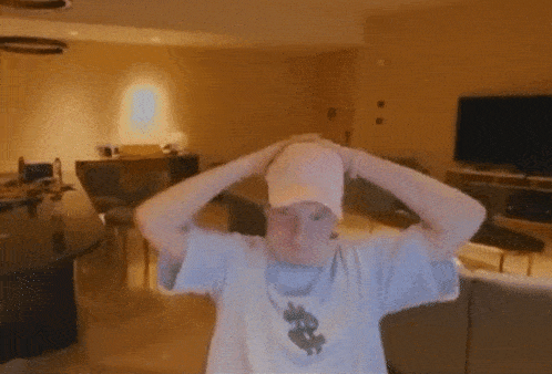 a man wearing a hat and a t-shirt with a dollar sign on it is holding his head in a living room .