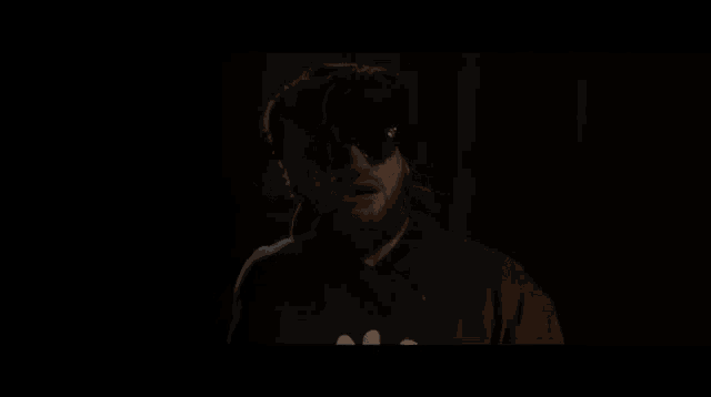 a man with a beard wearing sunglasses and a hat is standing in a dark room .