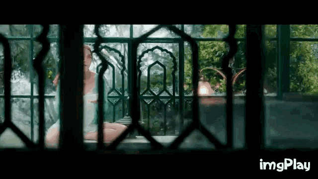a woman in a white dress is sitting on a balcony looking out a window .