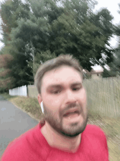a man with a beard is wearing a red shirt and white ear buds