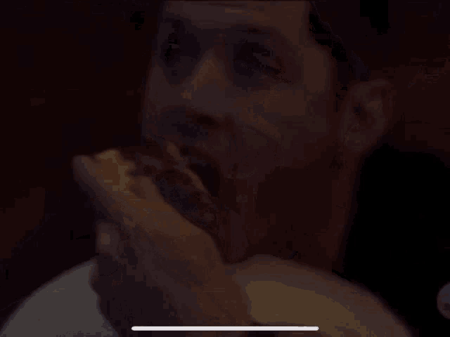 a man is sitting at a table eating a sandwich in a dark room .