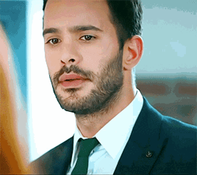 a man with a beard wearing a suit and tie looks at the camera