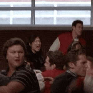 a group of people are sitting in a room with a man in a red jacket in the background