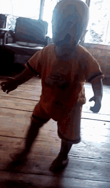 a child wearing a yellow shirt with cars on it is walking on a wooden floor