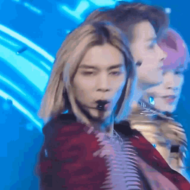 a man with long blonde hair is singing into a microphone while standing on a stage .