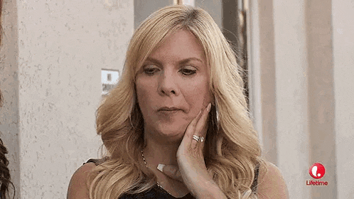 a woman with blonde hair is holding her hand to her face and looking at the camera .
