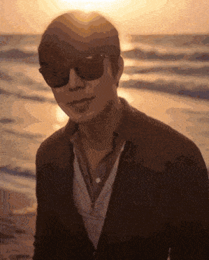 a man wearing sunglasses is standing on a beach at sunset