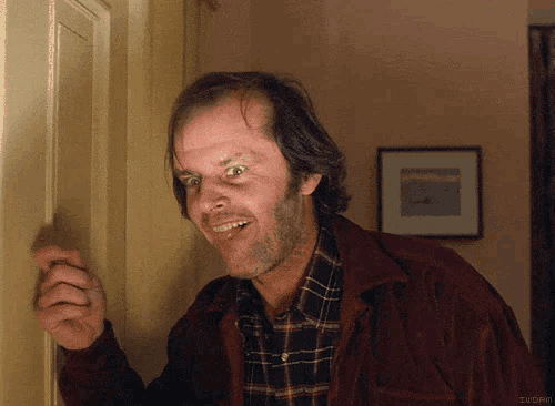 a man in a plaid shirt and a red jacket is smiling while looking through a door .