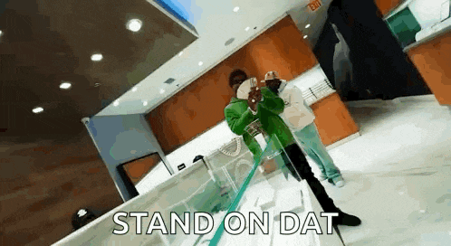 a man in a green jacket is standing in a room with the words `` stand on dat '' written above him .