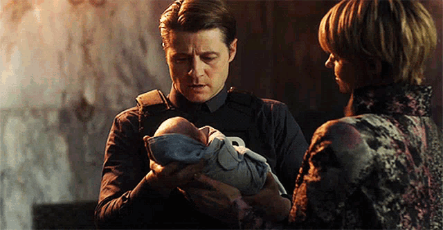 a man is holding a baby in his arms while a woman looks on .
