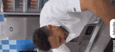 a man in a white shirt is leaning over a stove with a subscribe button on the bottom