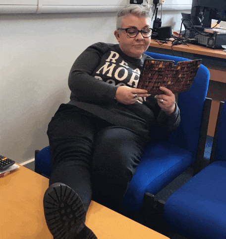a woman sitting in a chair reading a book and wearing a shirt that says mob