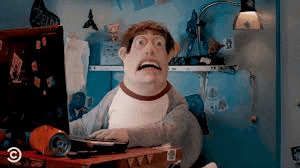 a cartoon character is sitting at a desk in front of a computer screen making a funny face .