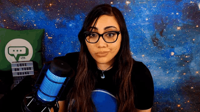 a woman wearing glasses stands in front of a microphone with a sign that says love on your ohana