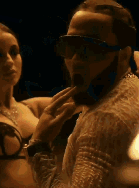 a man wearing sunglasses is standing next to a woman in a bra .