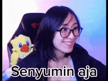 a woman wearing glasses sits in a chair next to a stuffed animal and the words senyumin aja