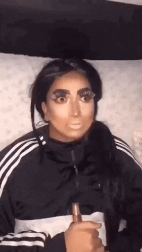 a woman in a black and white adidas jacket is holding a bottle of makeup .
