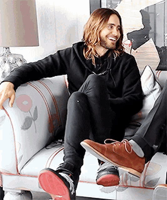 a man in a black hoodie sits on a white couch