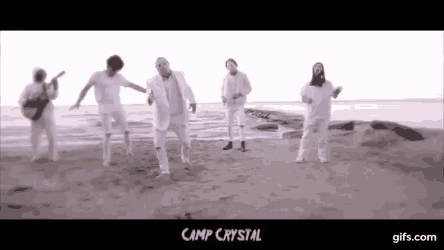 a group of people in white clothes are standing on a sandy beach .